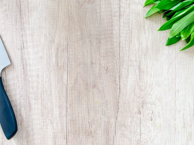 A bunch of fresh basil on a wooden cutting board beside a chef's knife