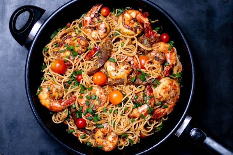 A pan of spaghetti, shrimp, cherry tomatoes and scallions, photographed from above